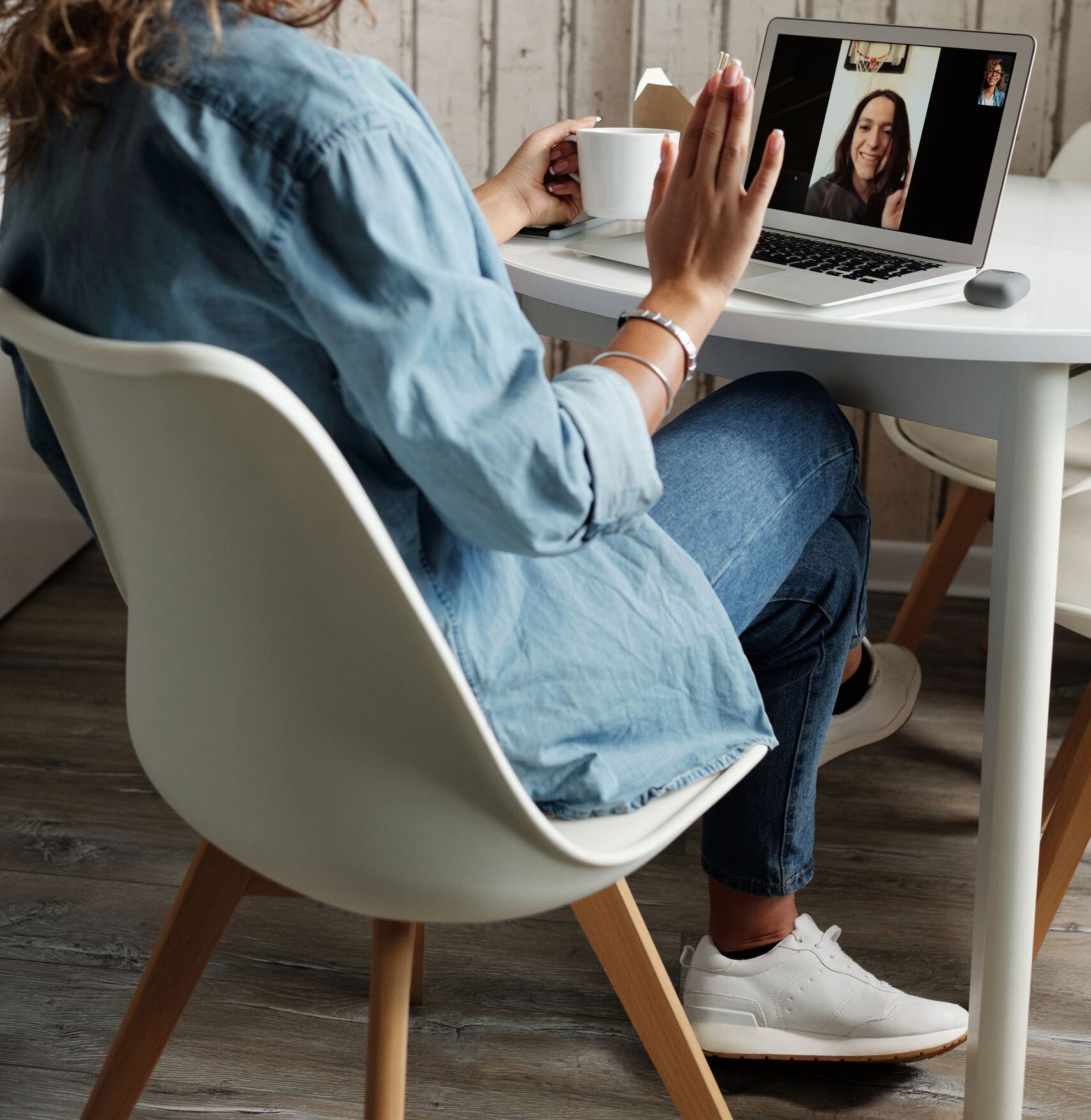 A woman in a blue shirt interacts on a video call using a laptop in a cozy home setting.