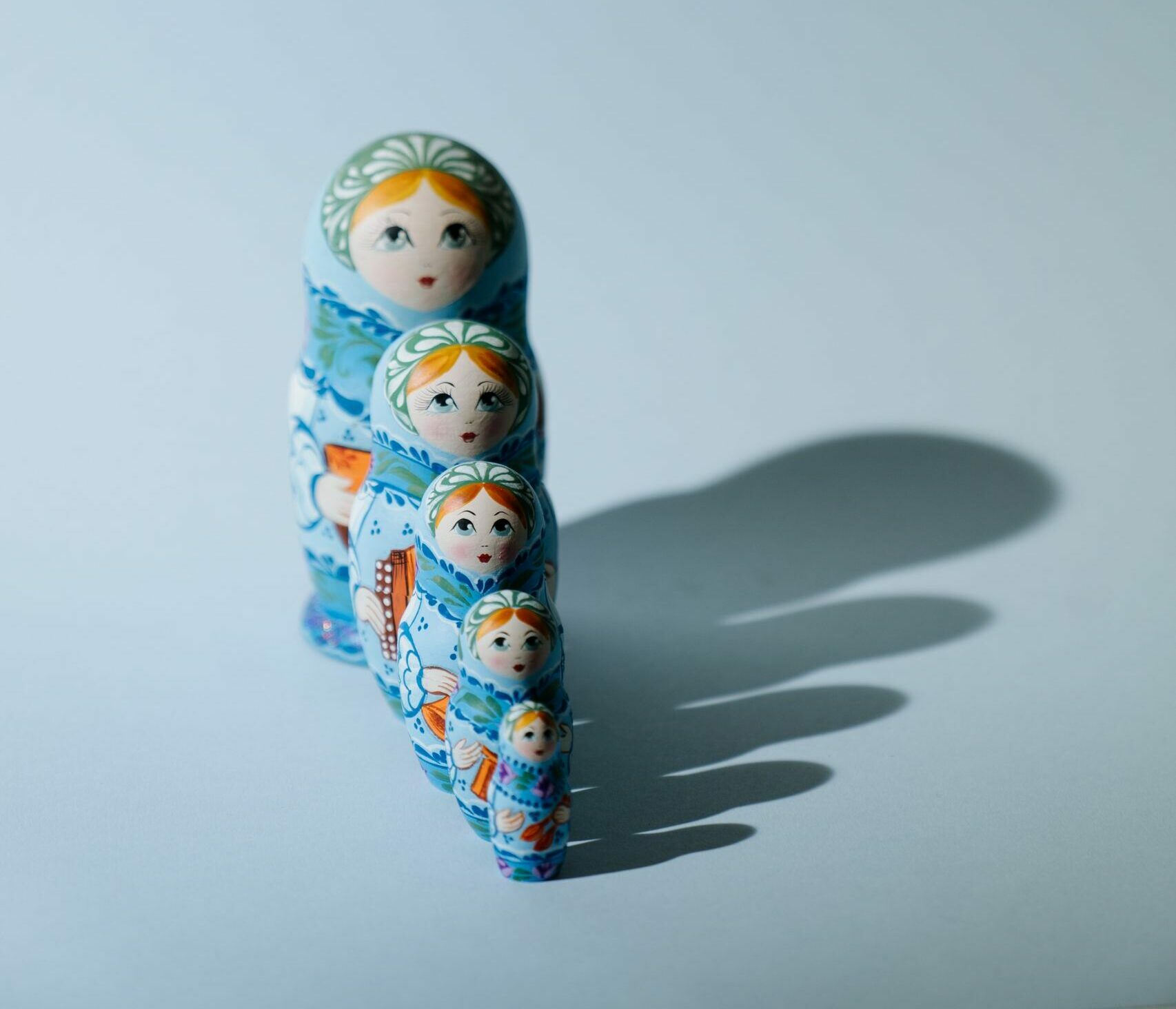 A set of Russian nesting dolls in blue casting a shadow on a light background.