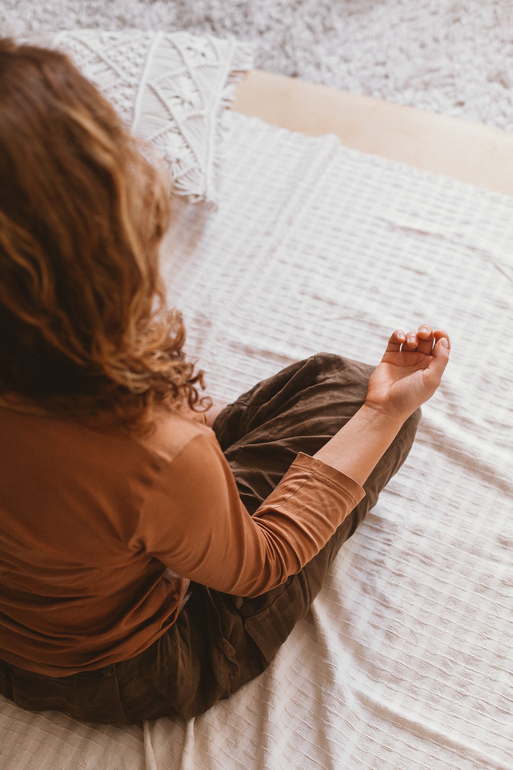 A woman in brown attire meditates on a soft surface indoors, promoting peace and mindfulness.