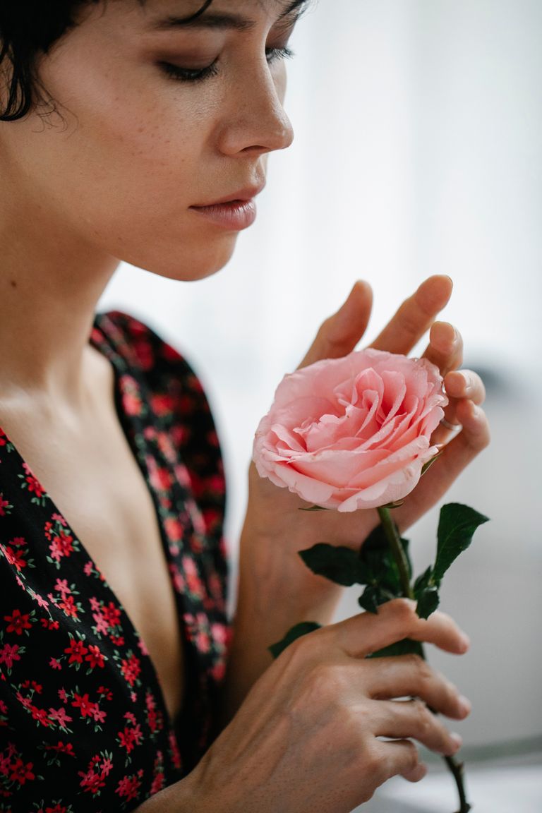 A serene portrait of a woman admiring a pink rose, embodying elegance and beauty.