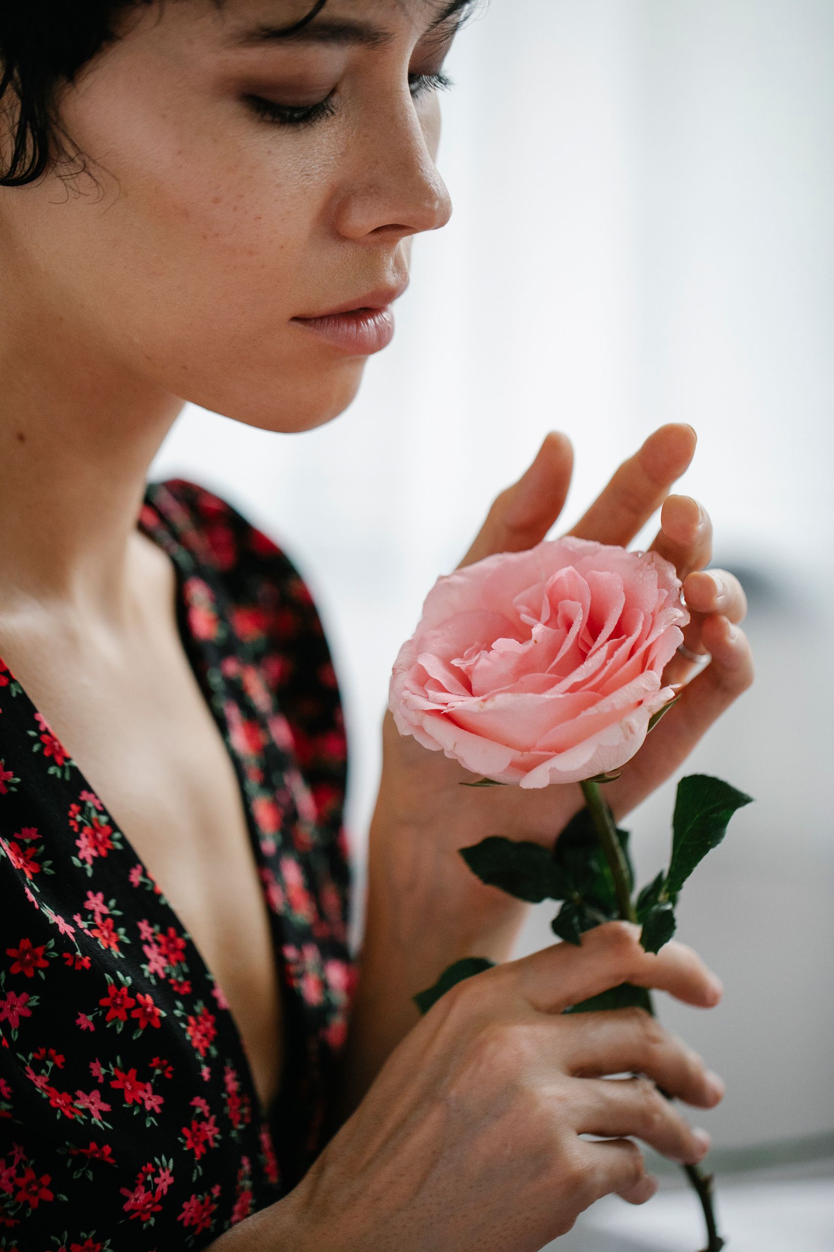 A serene portrait of a woman admiring a pink rose, embodying elegance and beauty.