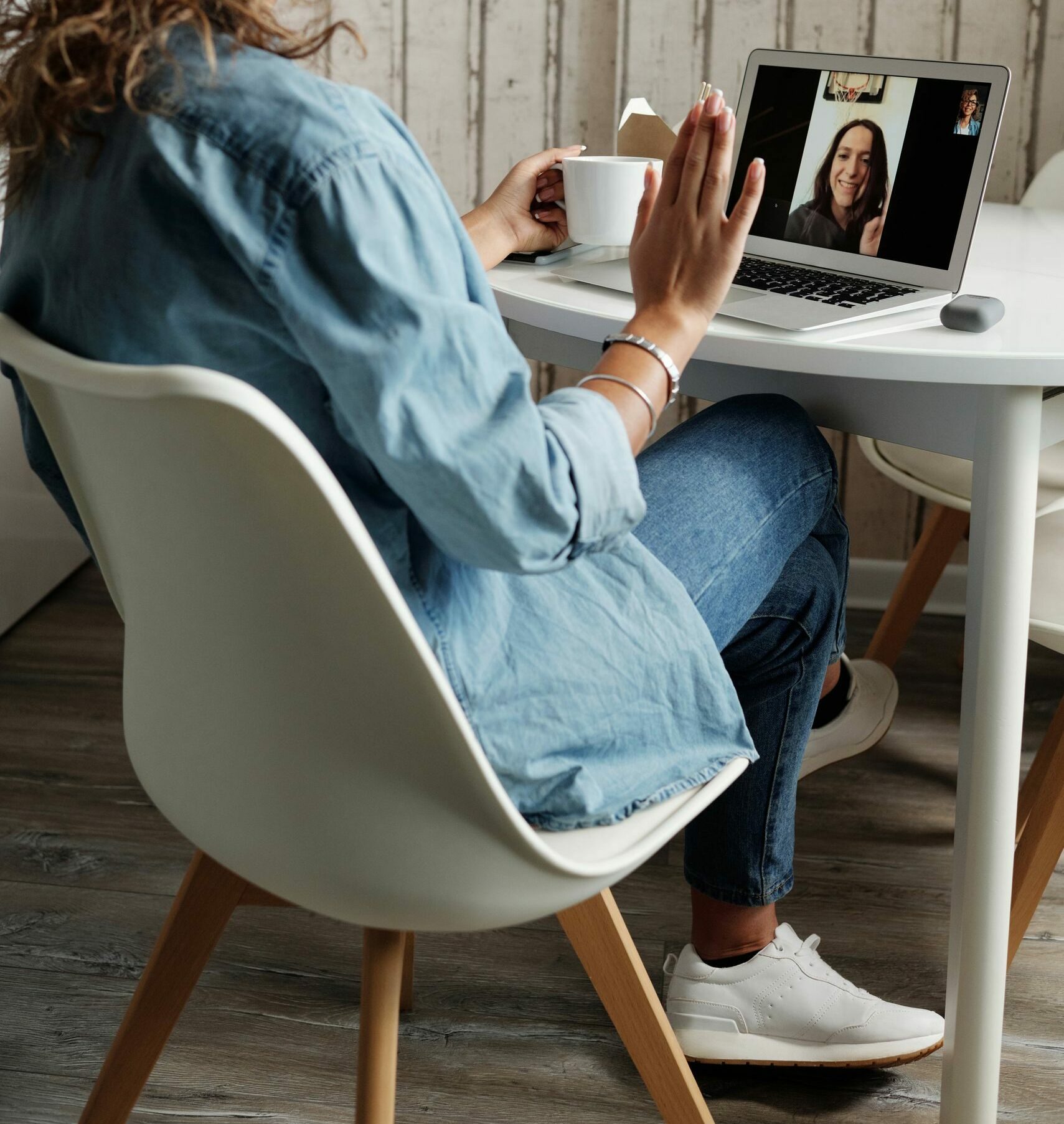 A woman in a blue shirt interacts on a video call using a laptop in a cozy home setting.